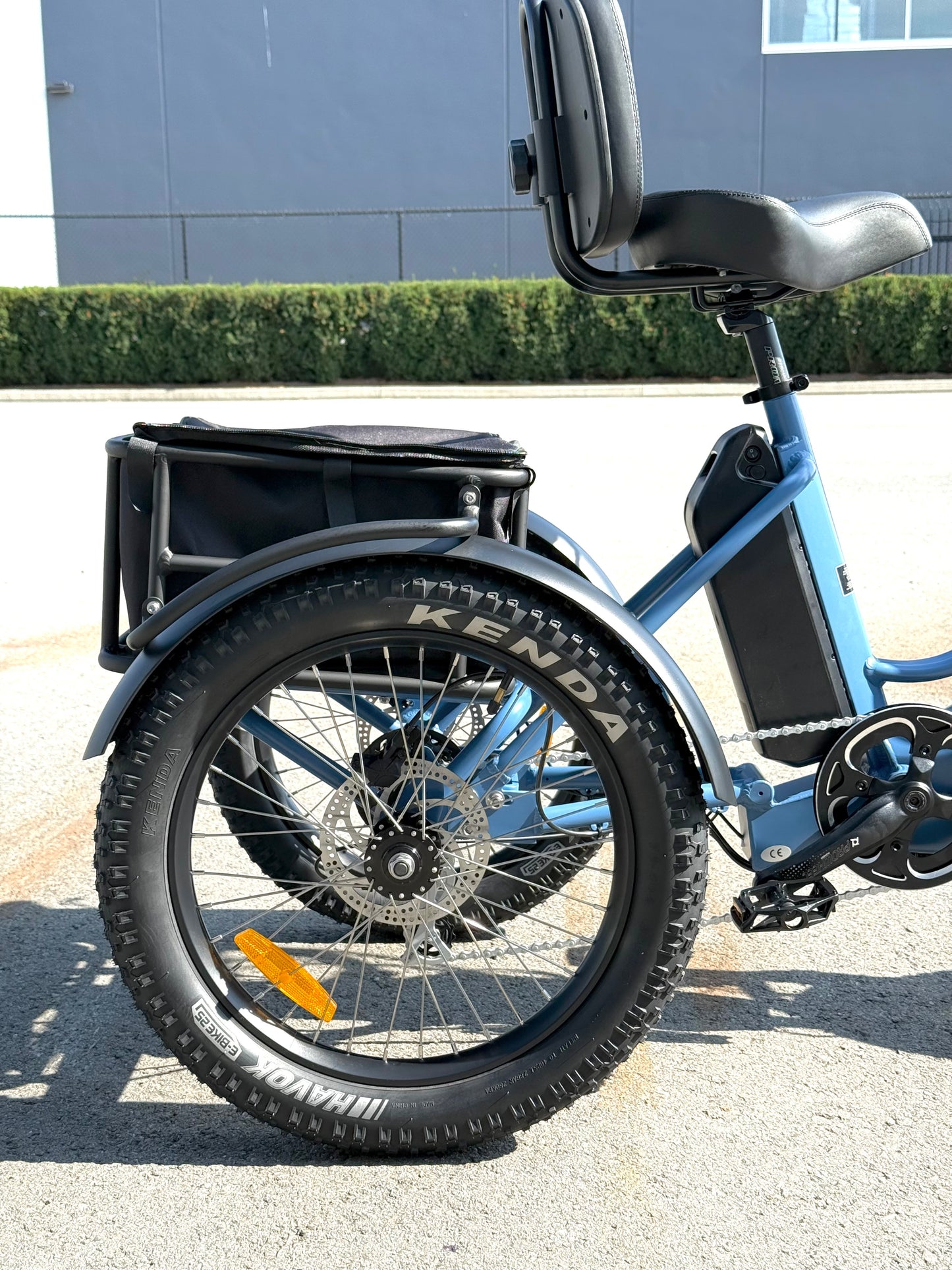 Blue electric tricycle with a black seat and cargo box on a paved surface.